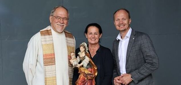 Ein Priester mit einer Frau und einem Mann, lächelnd mit Madonnafigur.